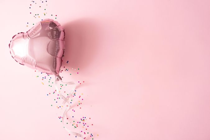 Pink foil balloon and confetti against pink background