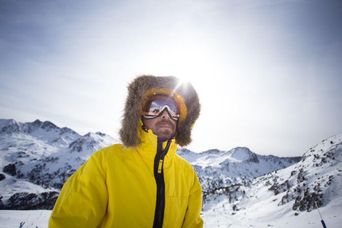 Man in yellow parka and goggles in ski resorts with sun flare