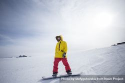 Man in yellow parka on top of mountain with snowboard 5nDD8b