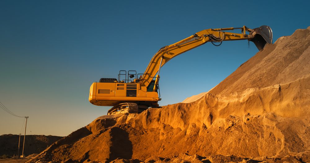 Construction Site On A Sunny Day: Industrial Excavator Digging Sand To Lay Foundation for Building New Apartment Complex. Workers Operating Heavy Machinery To Complete A Real Estate Project On Time.
