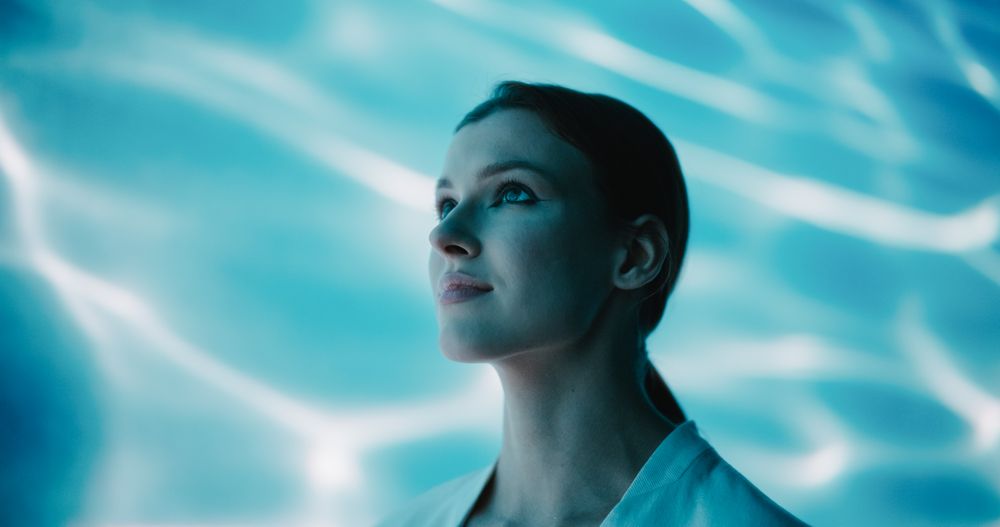Captivating Beauty Shoot: Young Female Model in Minimalistic White Coat Standing in a Room Abstract Water Background.