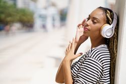 Female leaning on wall outside and listening to headphones on sunny day