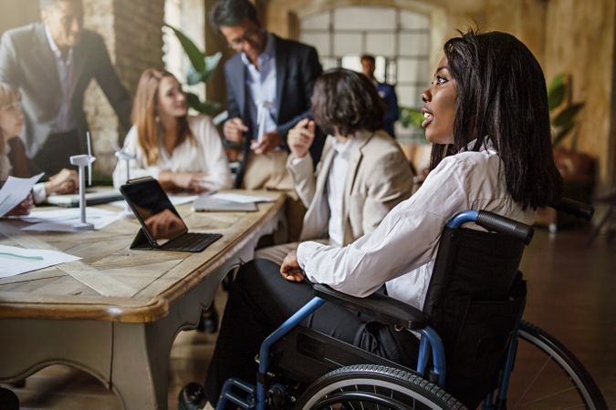 Office coworkers in the meeting room - main focus on Black woman in a wheelchair