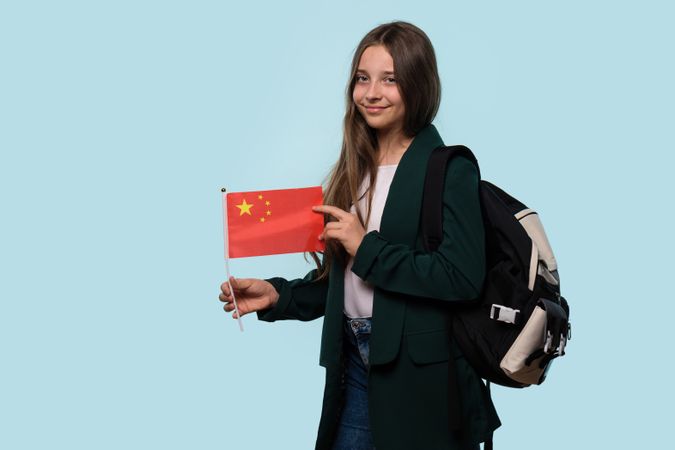Teen girl holding Chinese flag, with backpack, casual look.