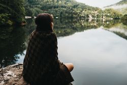 Woman sitting with blanket near lake and mountains