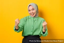 Smiling Muslim woman in headscarf and green blouse with both hands in celebratory fists 5wexmb