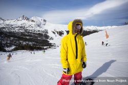 Man in yellow parka on mountain with snowboard 0JQQrb