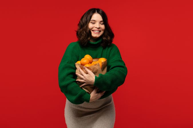Woman holding large paper bag full of fresh tangerines