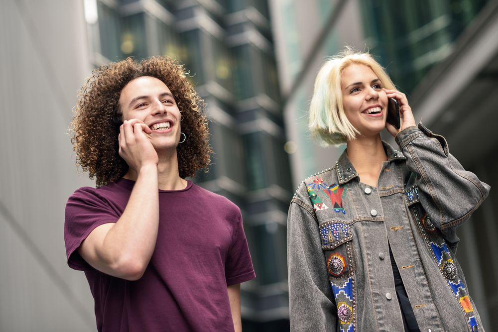 Male and female talking on cell phones walking on British city street