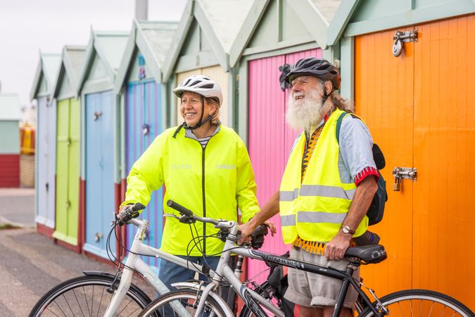 Two smiling older people standing with bikes looking away by colorful sheds