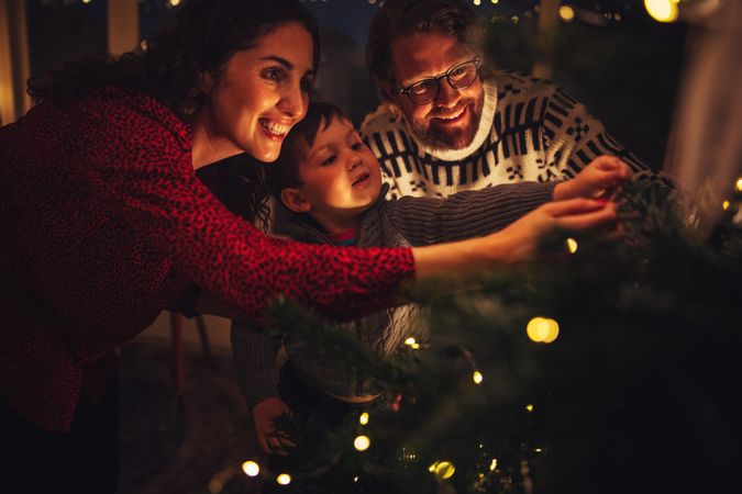 Small family smiling and decorating Christmas tree together