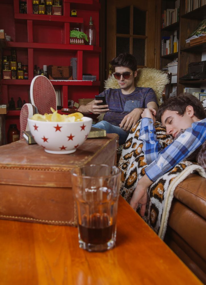 Young man sleeping on sofa and friend looking smartphone