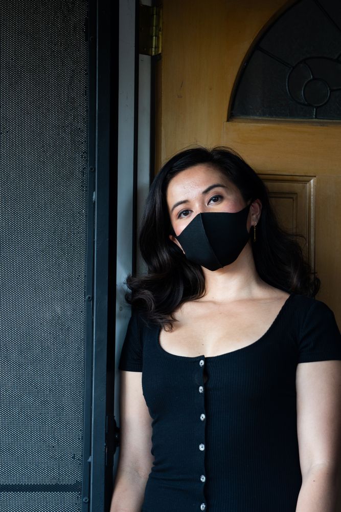 Portrait of woman at doorway at home in PPE mask looking at camera