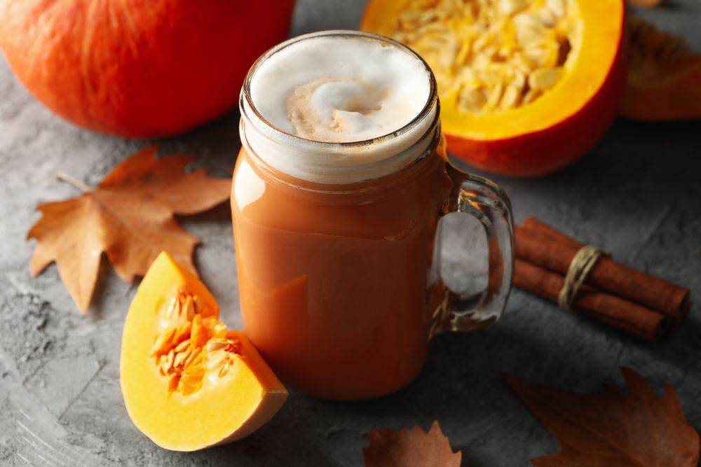 Composition with pumpkin latte, pumpkin, leaves and cinnamon on gray table