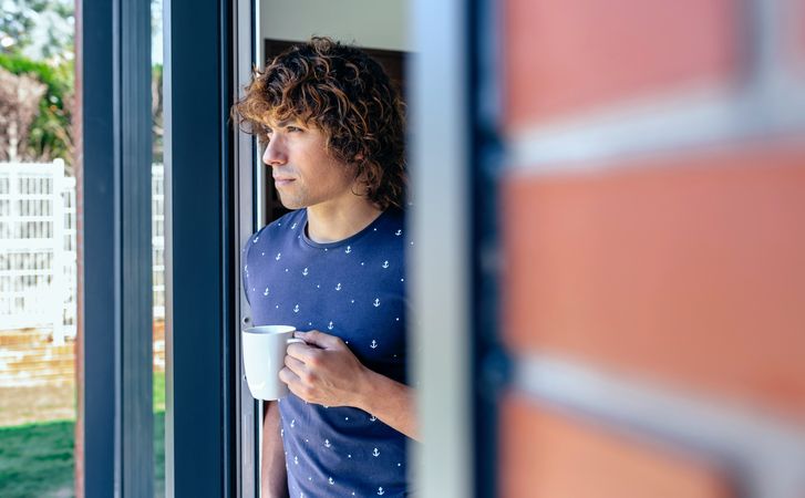 Man drinking coffee leaning against the window frame