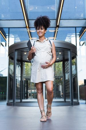 Smiling Black woman with laptop coming out of office building