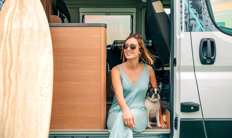 Smiling woman relaxing on stoop of motorhome door with cute dog