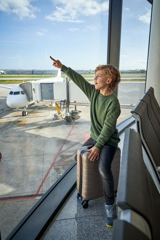 Happy kid pointing away sitting near window in airport terminal
