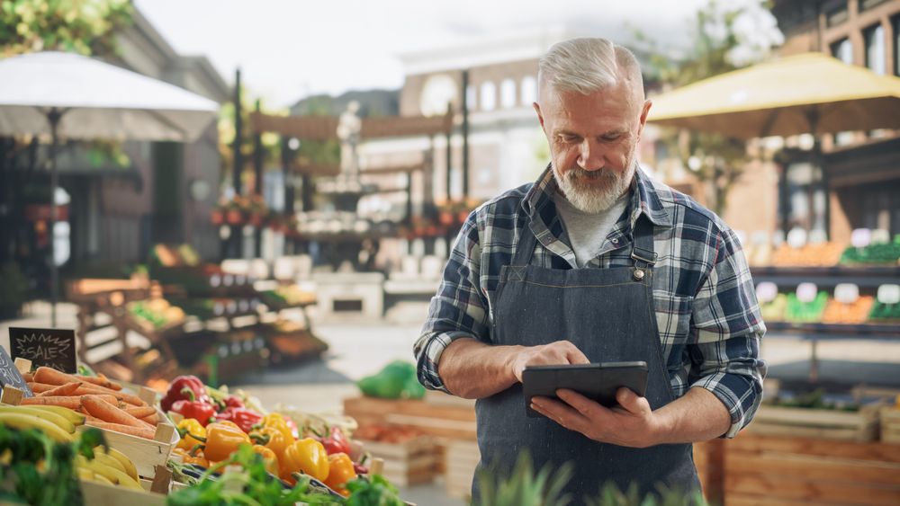 Portrait of an Adult Farmer Using Tablet Computer at Work while Selling Fresh Organic Agricultural Products From a Market Stall.