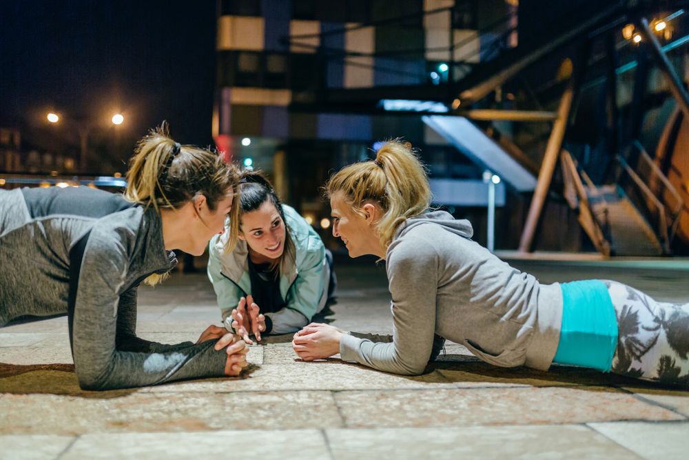 Female sport team doing planks during training in the city at night