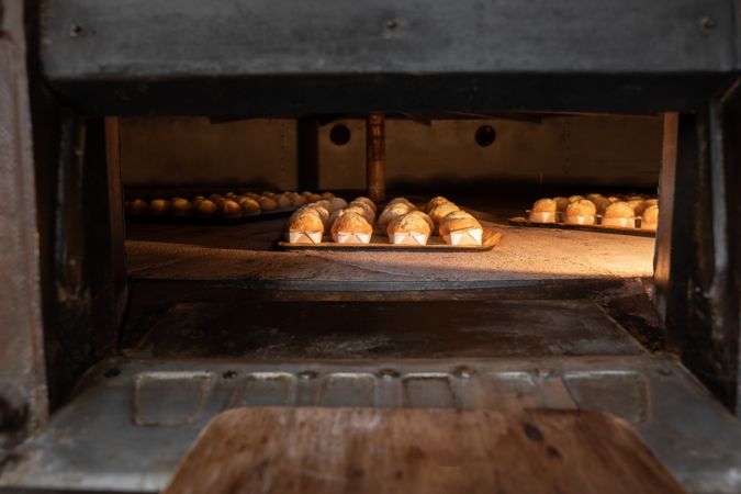 Some cupcakes are being baked inside of a big stone traditional oven