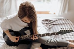 Brunette woman playing guitar on bed