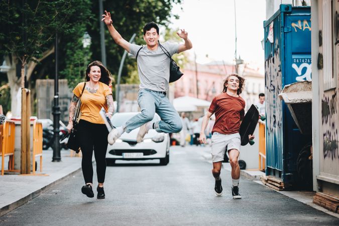 Funny multiracial friends having fun and running along city street