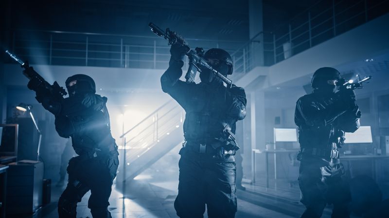Masked Squad of Armed SWAT Police Officers Stand in Dark Seized Office Building with Desks and Computers.