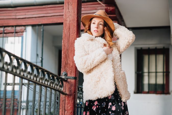 Smiling woman in warm wear standing near building and fence