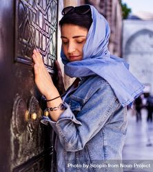 Woman in blue veil and denim jacket standing in front of wood carved wall beBvP0