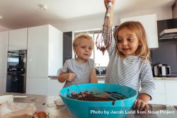 Little girl  whipping chocolate cream with whisk in bowl with brother supervising in kitchen 5nPK6b