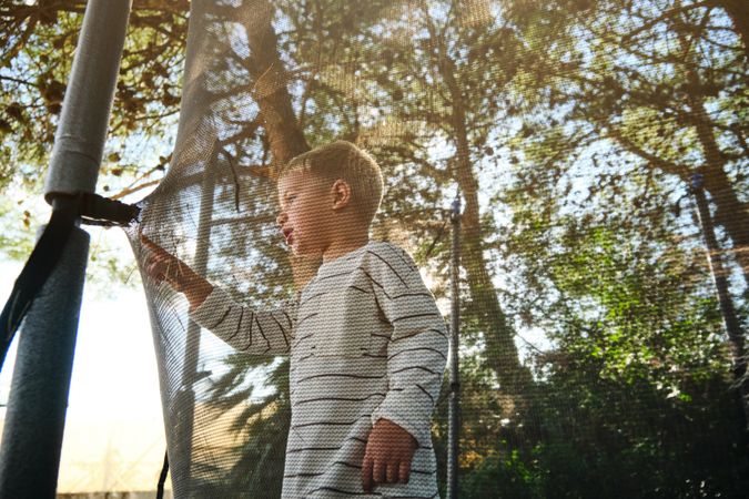 Boy standing and touching trampoline net in park