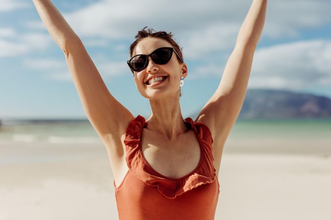 Tourist woman in sunglasses enjoying at beach with arms raised