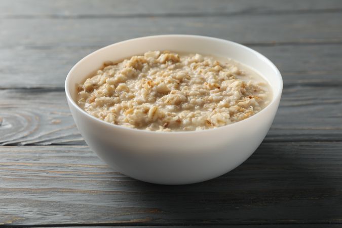 Bowl with oatmeal porridge on wooden background