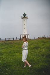 Woman walking in green meadow near lighthouse
