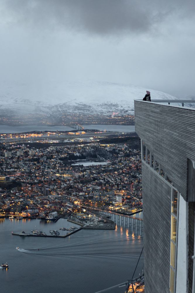 Tourists enjoying wonderful view of city against snowy mountain standing on viewpoint in evening