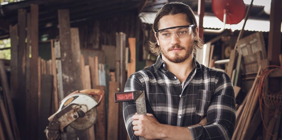 Portrait of male woodworker wearing safety glasses and holding tool in workshop