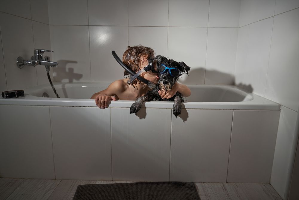 Boy kissing dog in bathtub