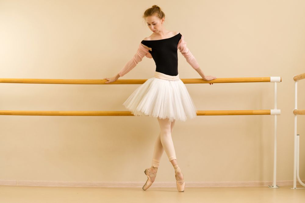 Ballet dancer practices on pointe, holding barre for balance