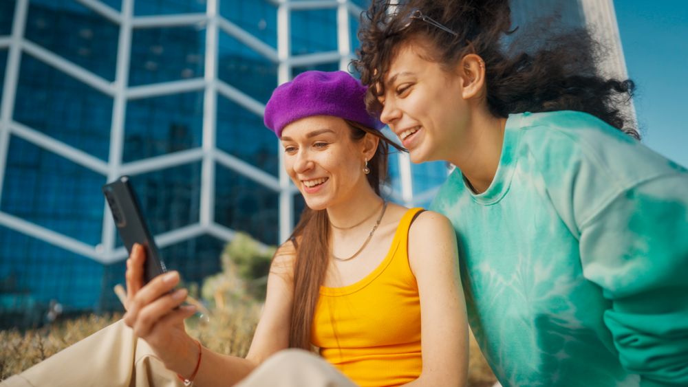 Two Joyful Young Women Sharing A Moment Over A Smartphone
