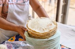 Crop baker putting pile of flatbreads in cloth bag at stall