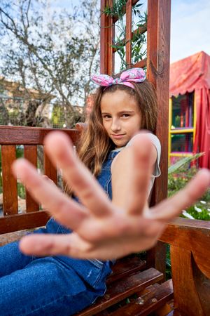 Happy girl in headband reaching out hand on bench in garden