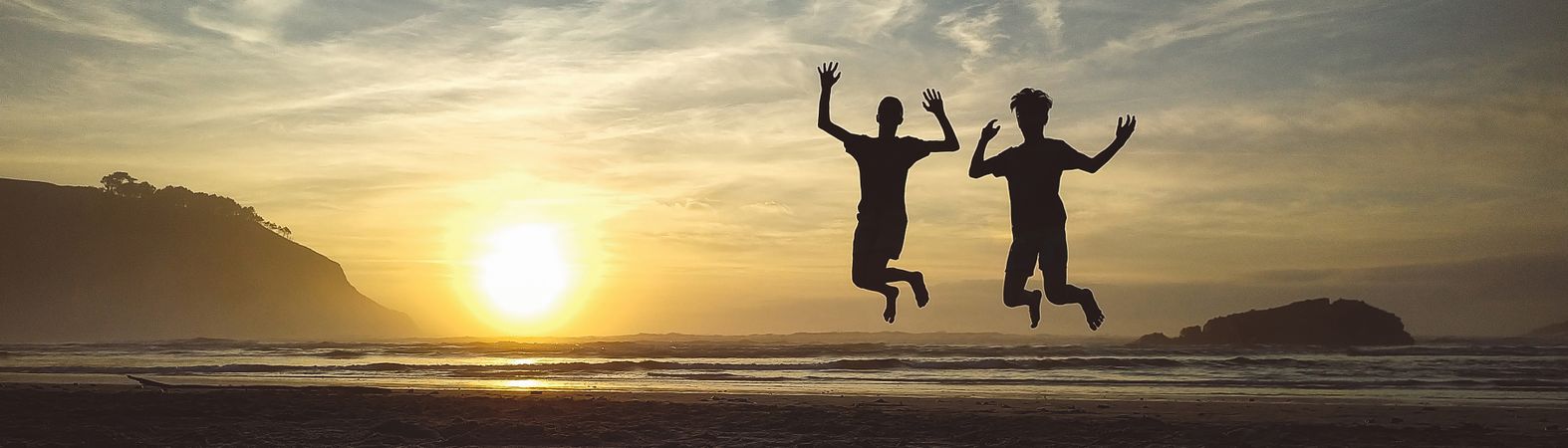 Silhouettes of two kids jumping in the beach at sunset