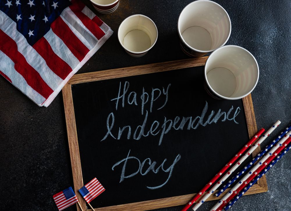 Top view of chalkboard with the words "Happy 4th of July" with American flags and drink straws and cups