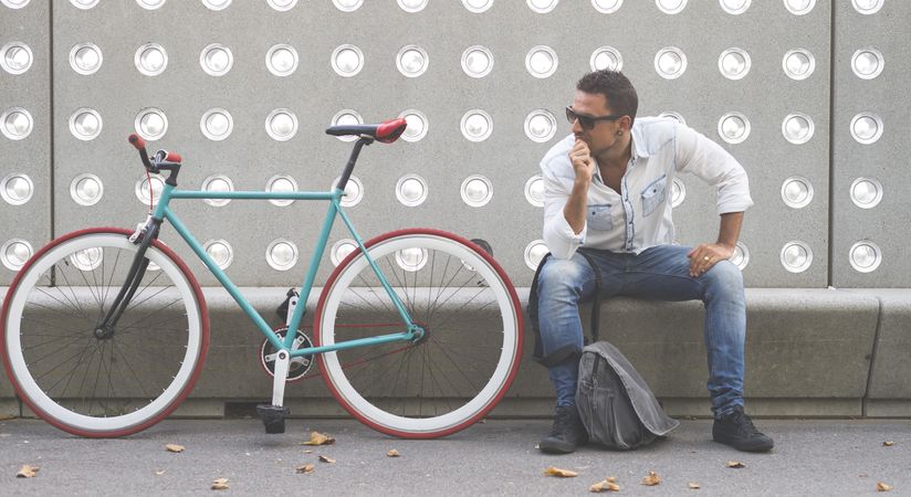 Curious male sitting with bike parked in front of patterned cement wall