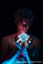 Topless young man holding crystal ball lamp against dark background beMeGb