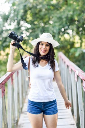 Happy woman walking with SLR camera, wearing straw hat outside, vertical