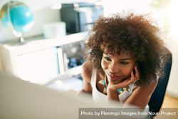 Looking down at curly haired female at her home office desk reading computer screen 0W3lp0