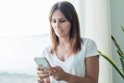 Woman checking phone sitting next to window