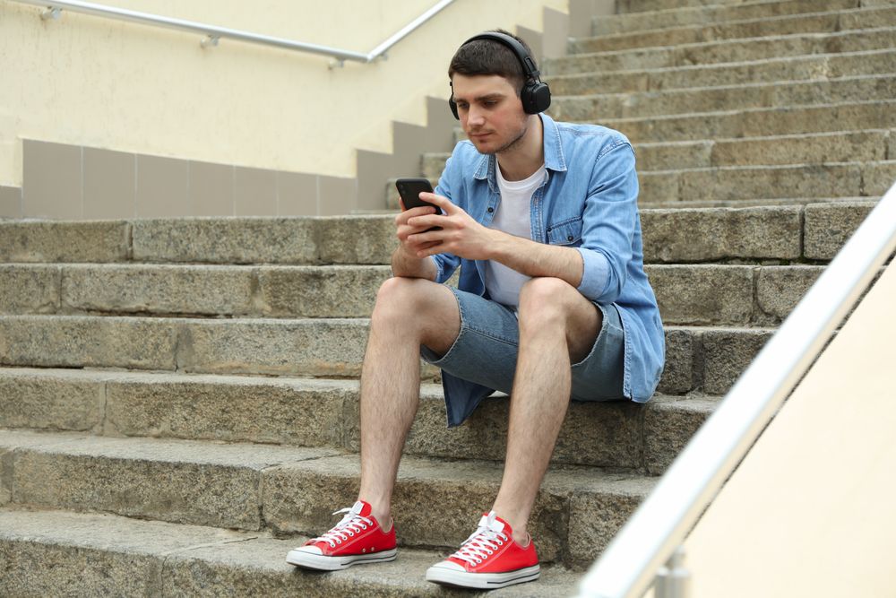 Young man in headphones sits on the steps and looking in phone